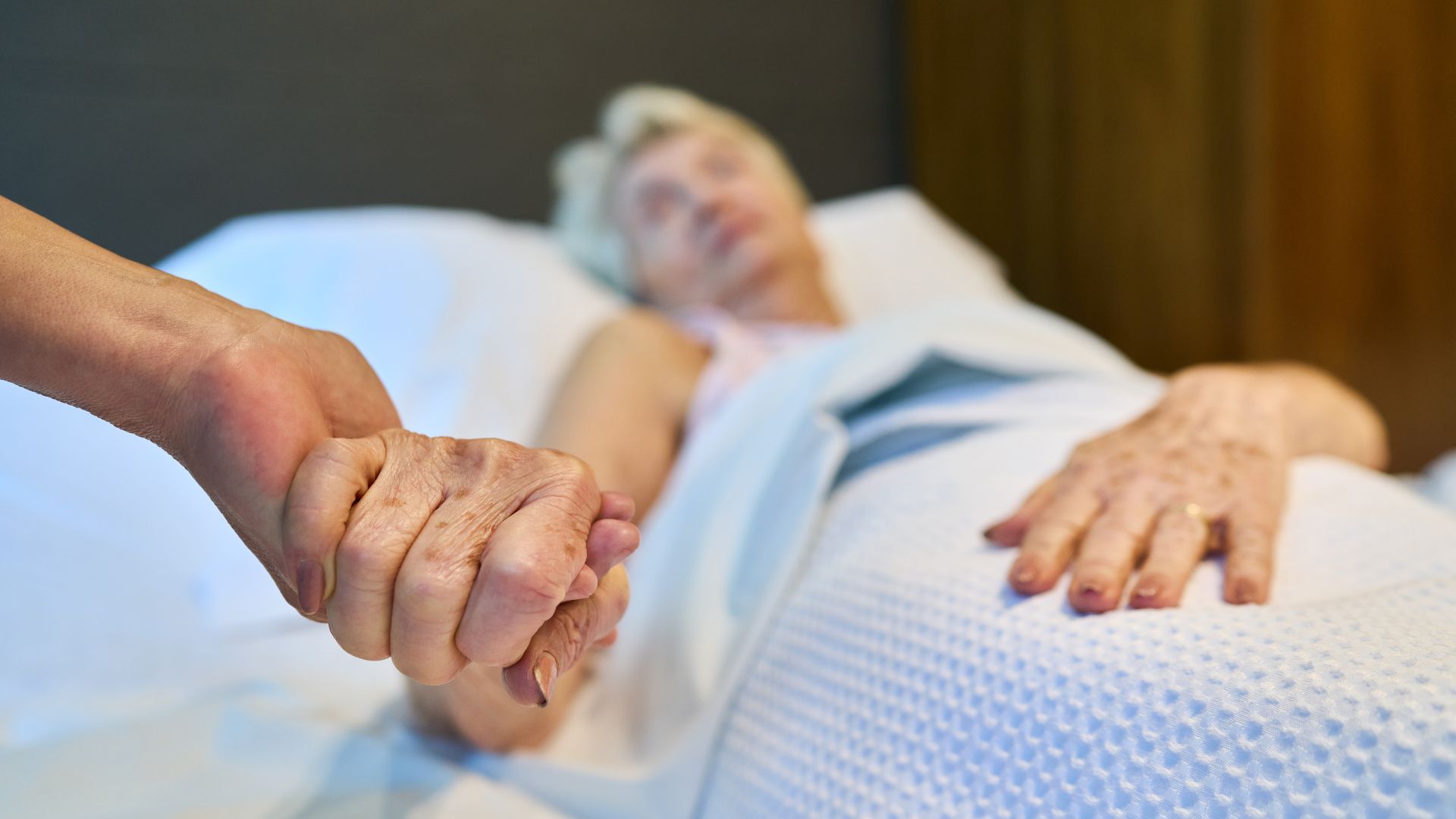 Elderly woman in a skilled nursing facility receiving compassionate support while holding hands with a caregiver.